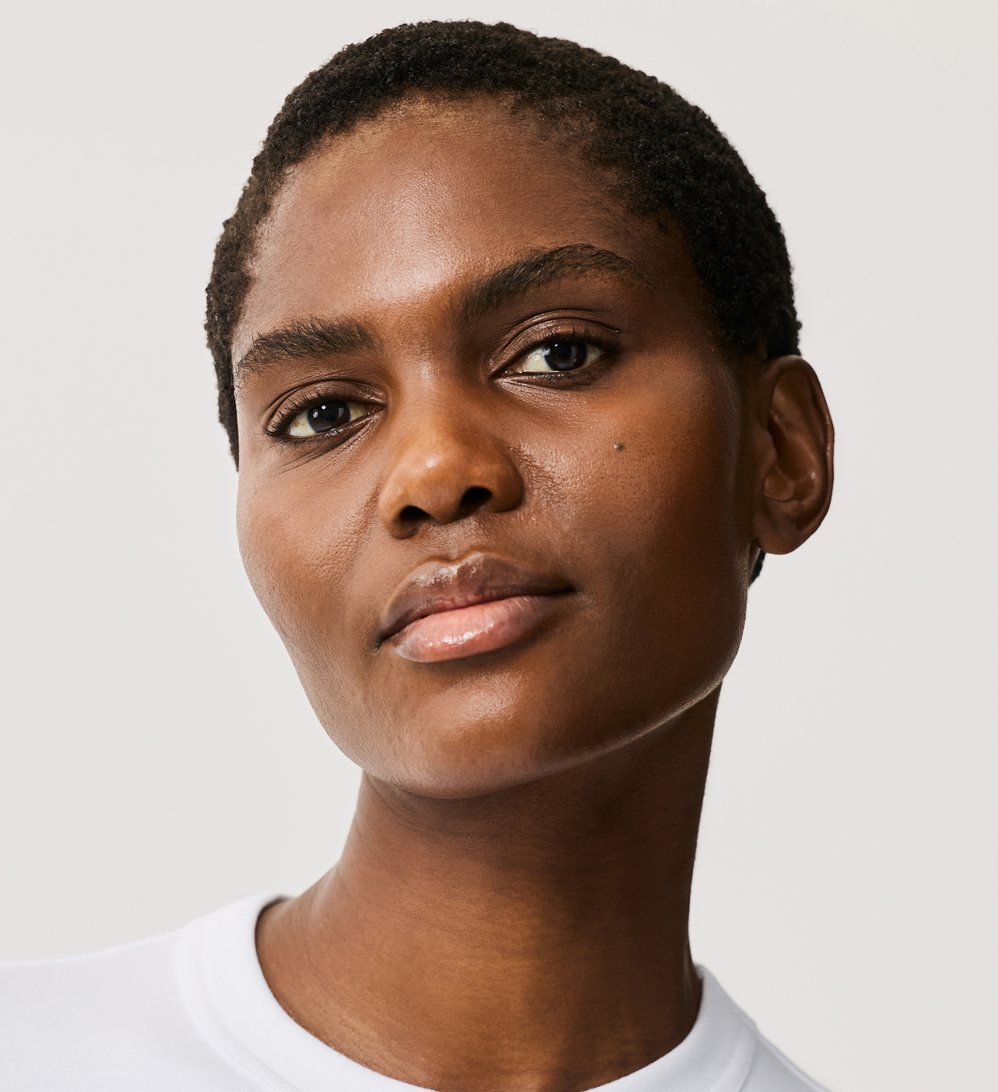Model wearing and holding Hydraveil Serum Foundation in shade 18 against a neutral background