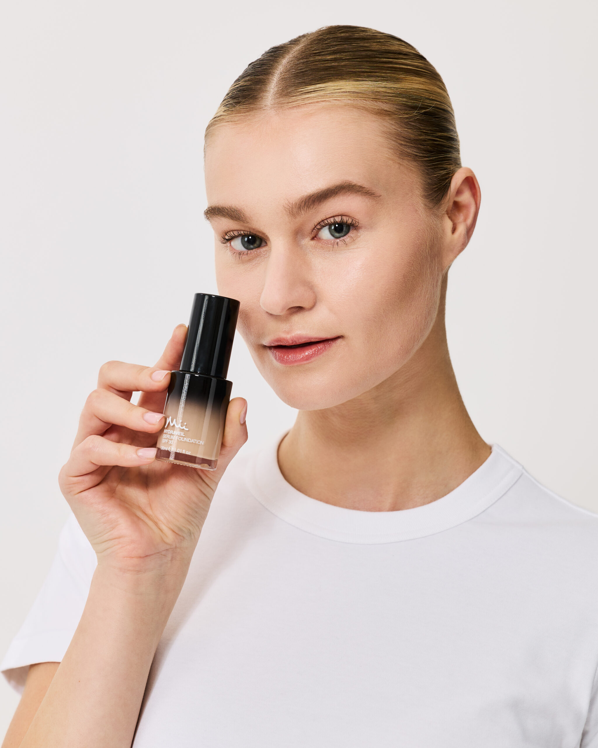 Model wearing and holding Hydraveil Serum Foundation in shade 3 against a neutral background