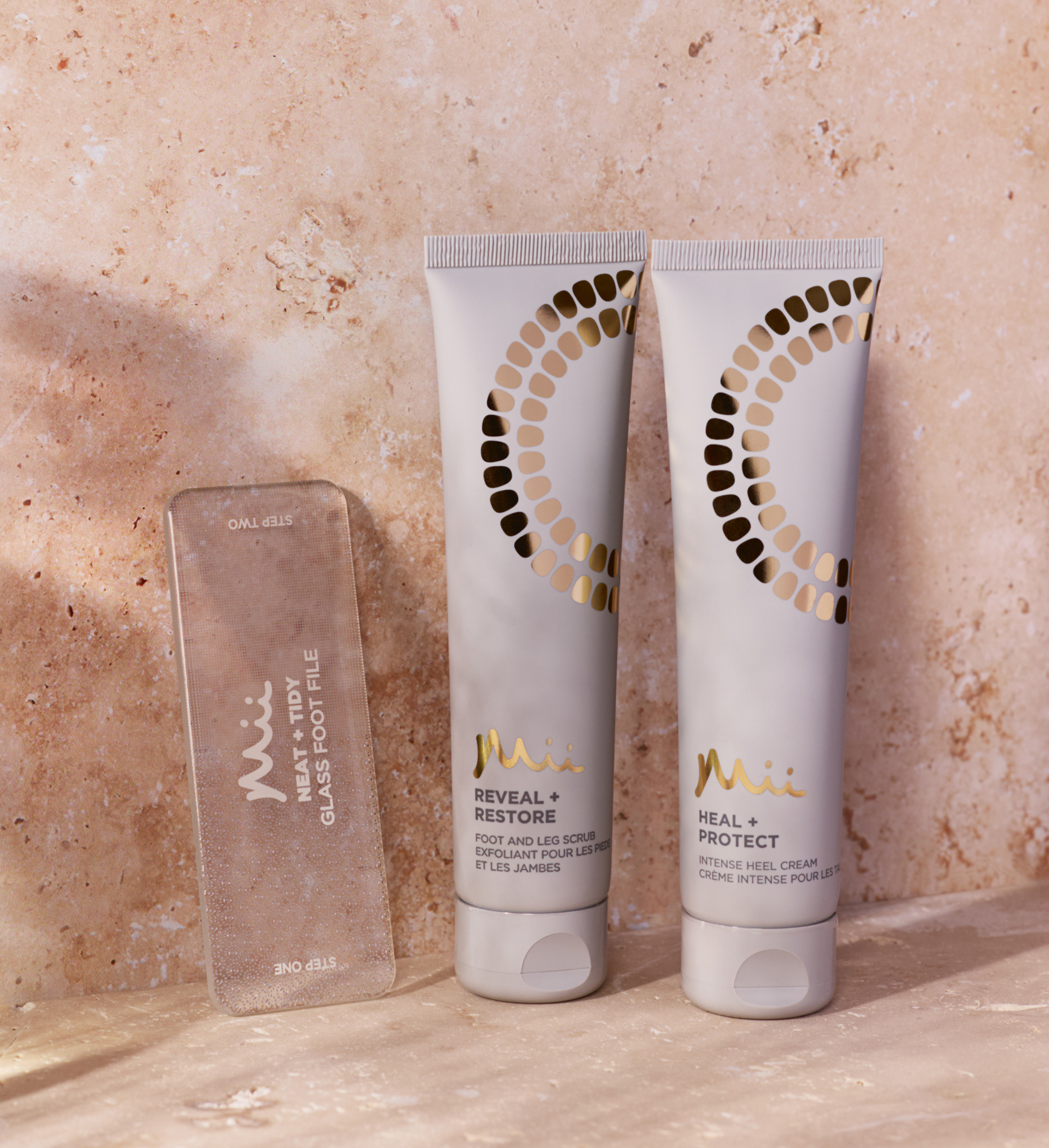 Reveal + Restore Foot Scrub 100ml, Neat + Tidy Glass Foot File and Heal + Protect Intense Heel Cream 100ml against a marble background